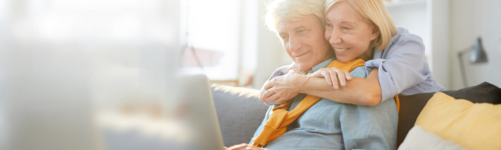 older couple hugging on couch looking at laptop