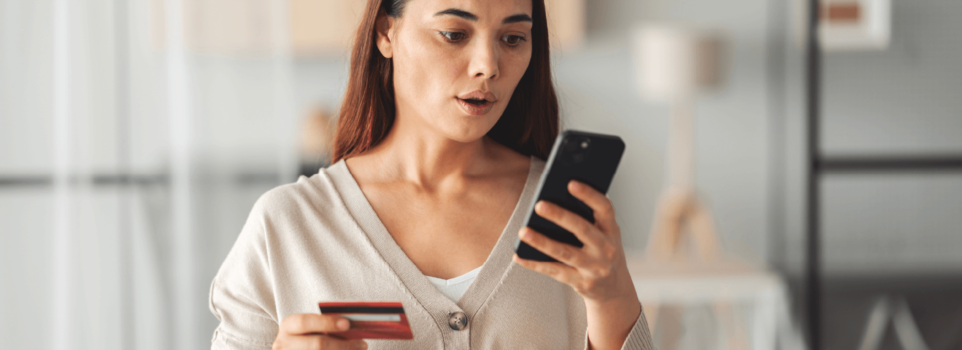 Shocked woman looking at her bank statement online while holding her debit card